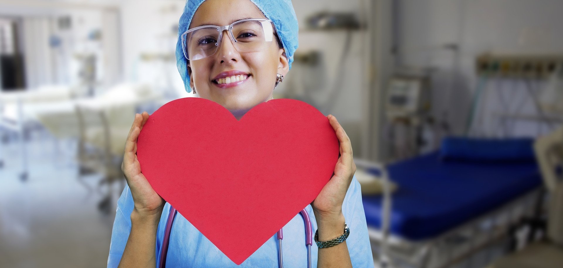 Krankenschwester die ein rotes Herz in die Kamera hält und lächelt