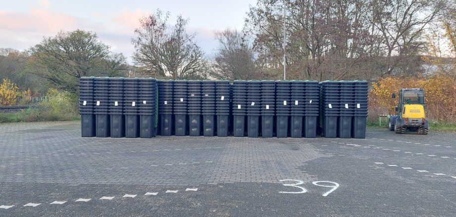 Ein Parkplatz mit vielen Stapeln an schwarzen Tonnen mit grünem Deckel