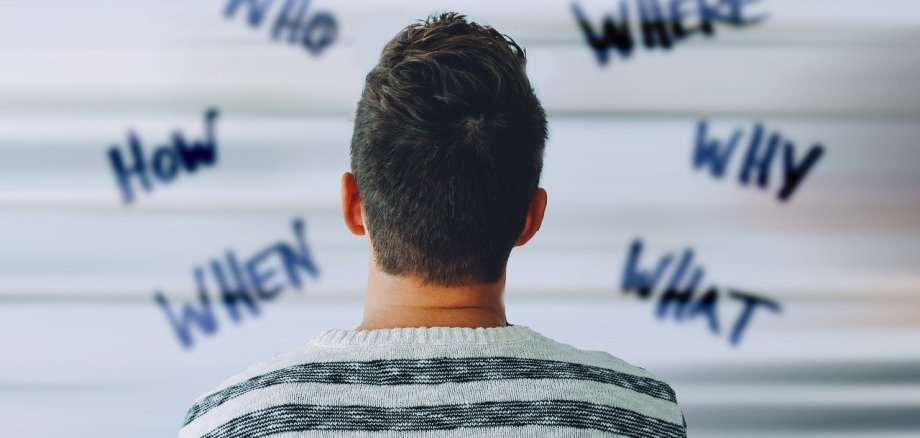 Beratung Kopf Fragen Ein junger Mann schaut auf eine Wand mit Fragen