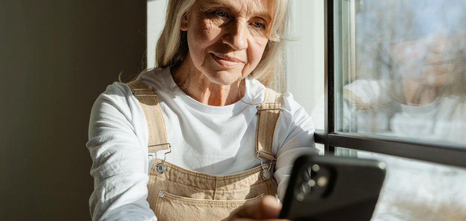 Seniorin mit Mobiltelefon Eine Seniorin sitzt mit Mobiltelefon am Fenster