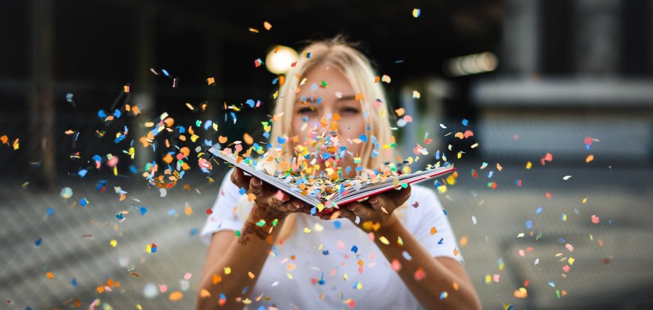 Konfettibuch Eine Frau bläst Konfetti von einem Buch in die Kamera