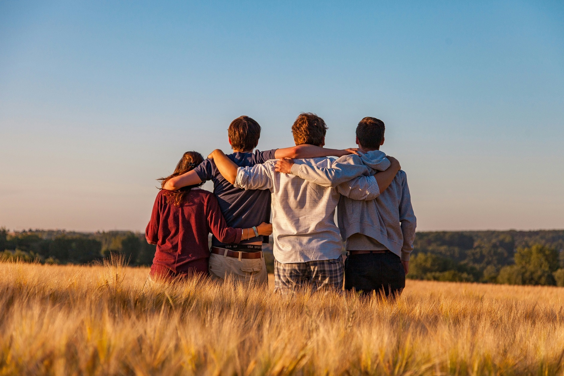 Vier Jugendliche blicken in die Zukunft Vier Jugendliche von hinten in einem Feld