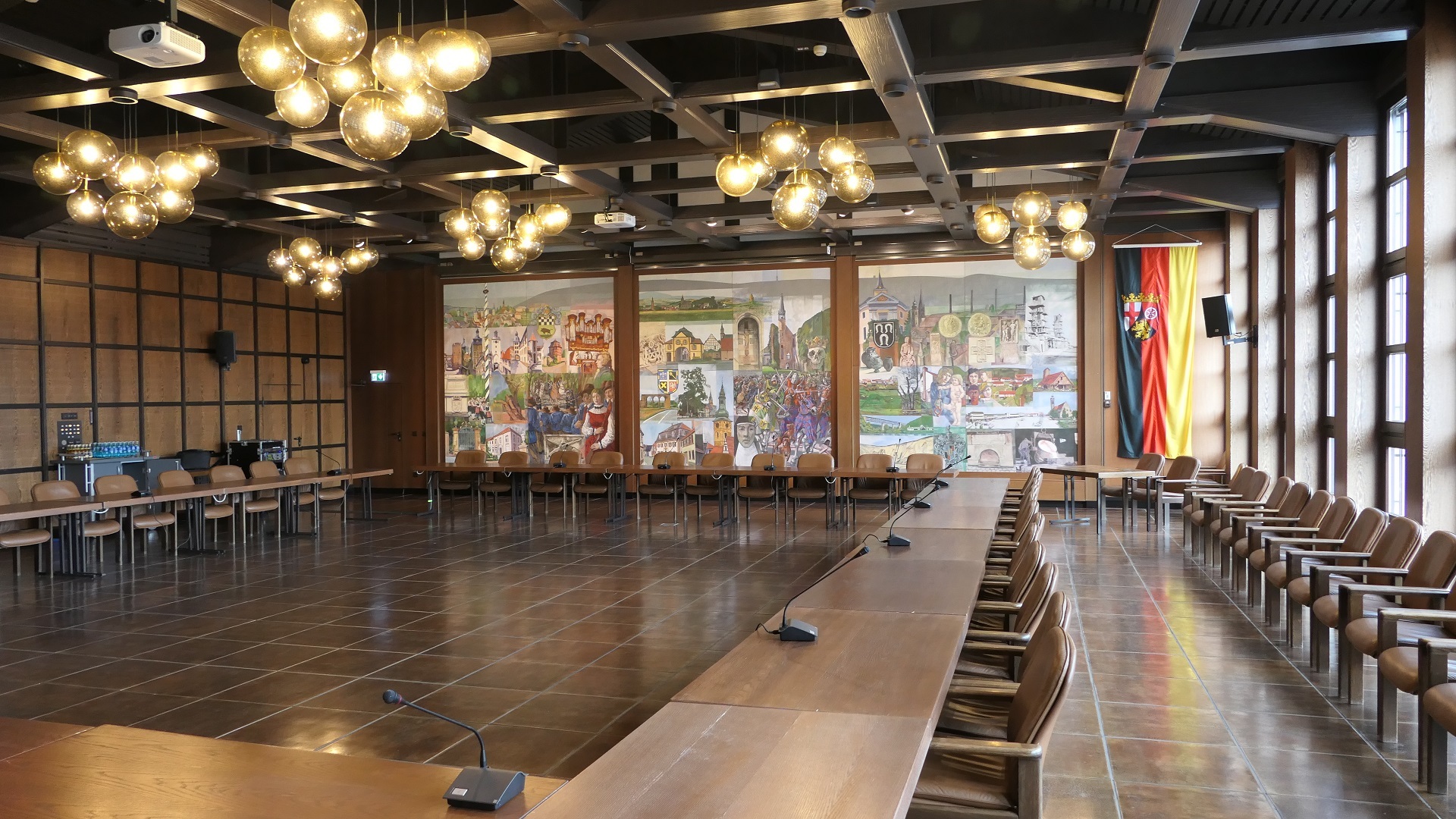 Der Große Sitzungssaal der Kreisverwaltung mit Sitzungsbestuhlung im Viereck. Auf der rechten Seite ist die Fensterfront, man sieht die Wandmalerei von Eisenberg und Kirchheimbolanden.