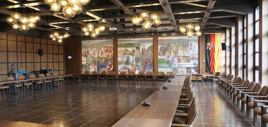 Der Große Sitzungssaal der Kreisverwaltung mit Sitzungsbestuhlung im Viereck. Auf der rechten Seite ist die Fensterfront, man sieht die Wandmalerei von Eisenberg und Kirchheimbolanden.