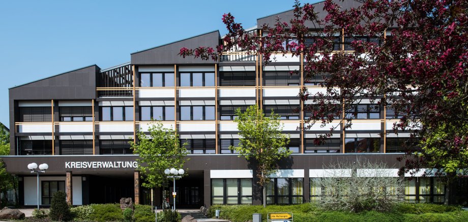 Kreishaus von der Uhlandstraße aus Das Kreishaus bei Sonnenschein von der gegenüberliegenden Straßenseite aus fotografiert. Im rechten Vordergrund sind noch Bäume zu sehen.