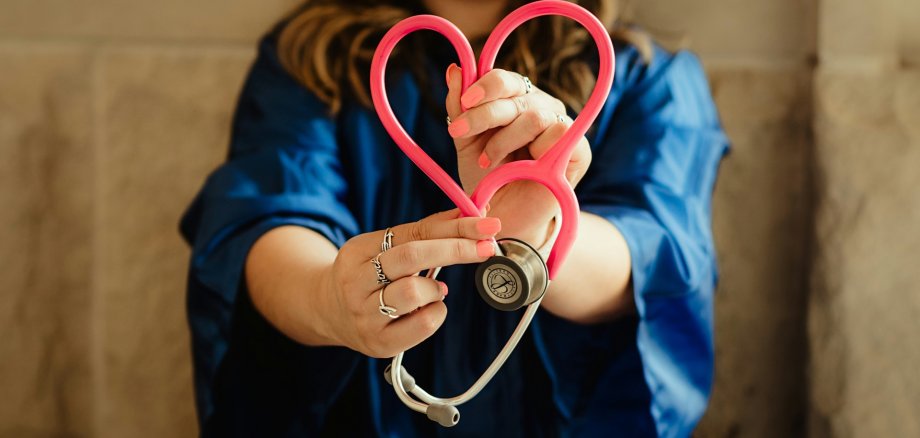 Ärztin mit Herz-Stethoskop Im Vordergrund ein Stethoskop, das in Herzform gehalten wird; im Hintergrund eine Ärztin