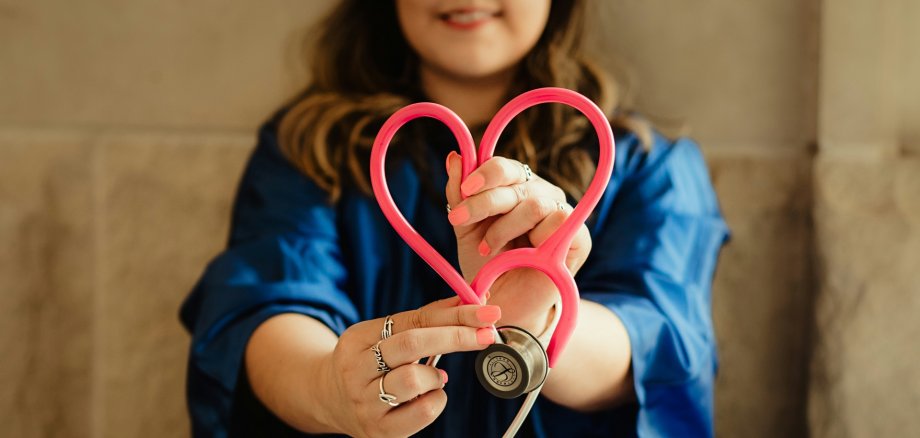 Ärztin mit Herz-Stethoskop Im Vordergrund ein Stethoskop, das in Herzform gehalten wird; im Hintergrund eine Ärztin
