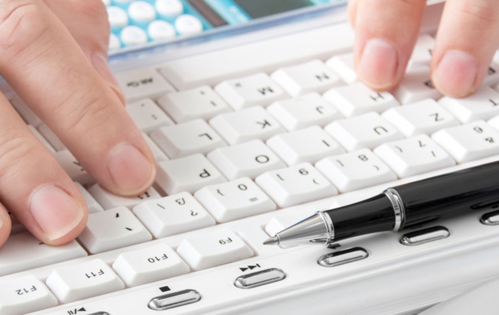 Finger auf einer weißen Tastatur, auf der ein Kugelschreiber liegt.