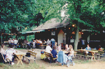 Bild von einer Feier vor der Waldhütte mit Leuten die an Bierbänken sitzen