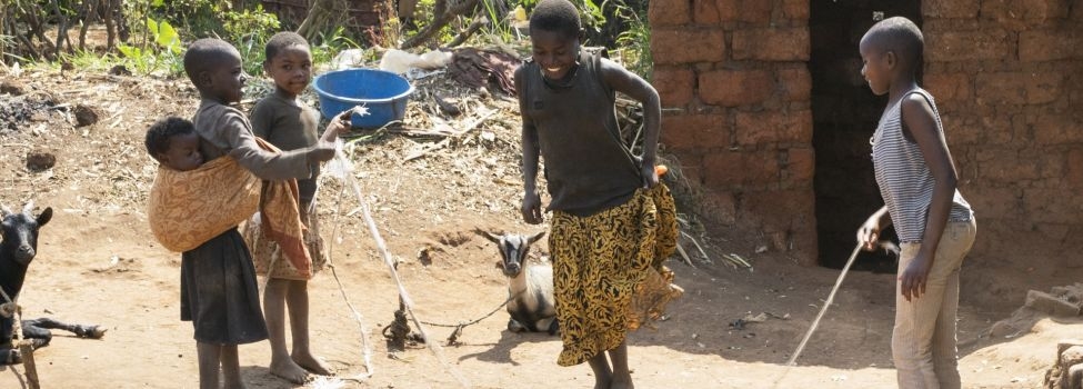 Spielende Kinder Vier Kinder spielen zusammen. Zwei halten ein Seil, eines springt gerade über das Seil. im Hintergrund liegt eine angebundene Ziege auf dem Boden.