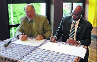 Der ehemalige Landrat Werner und der Ex-Bürgermeister und heutige Beauftragte des Distriktrates JB Bizimana unterschreiben einen Vertrag gemeinsam nebeneinander im großen Sitzungssaal in der Kreisverwaltung einen Vertrag.