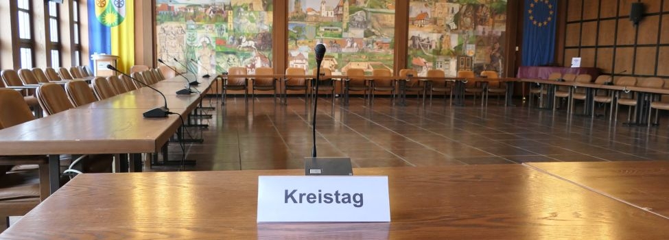 Das Schild mit der Beschriftung "Kreistag" steht auf einem Tisch mit einem Mikrofon im großen Sitzungssaal.